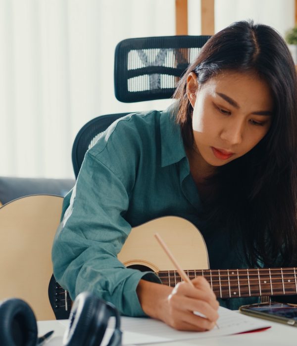 woman songwriter play acoustic guitar listen song from smartphone think and write notes.